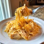 A fork lifts a cheesy, saucy portion of Chicken Spaghetti, showing melted cheese strings.