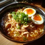 A close-up of a steaming bowl of Chicken Ramen topped with shredded chicken, scallions, and soft-boiled eggs.