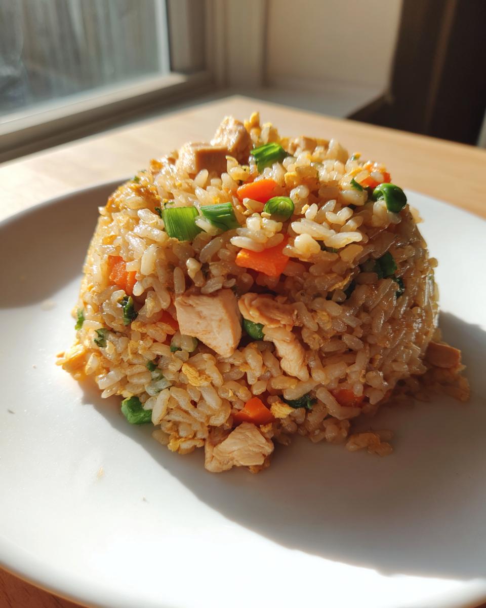 A perfectly molded serving of Chinese Chicken Fried Rice featuring rice, chicken pieces, carrots, peas, and green onions.