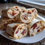 A stack of sliced Crack Chicken Pinwheels filled with chicken, cream cheese, and bacon, resting on a white plate.