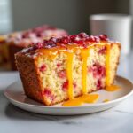Close-up of a slice of Cranberry Orange Glazed Cake topped with cranberries and dripping with orange glaze.