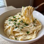 A fork lifting strands of fettuccine coated in rich Creamy Garlic Parmesan sauce, topped with parsley.