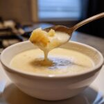 A spoonful of creamy, chunky Potato Soup being lifted from a white bowl.