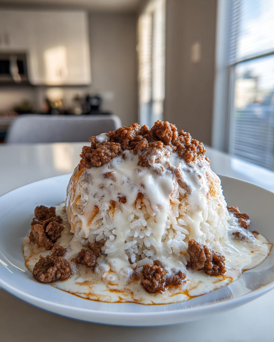 A mound of white rice topped with creamy queso sauce and seasoned ground steak, served in a white bowl.