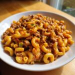 A close-up of a white bowl filled with Creamy Rotel Pasta With Ground Beef, featuring elbow macaroni in a cheesy, spicy sauce.