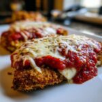 A close-up of a breaded cutlet topped with rich marinara sauce and melted mozzarella cheese, showcasing the perfect Chicken Parmesan.
