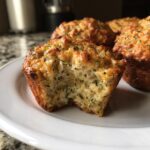 A close-up of a Crispy Parmesan Zucchini Muffin with a bite taken out, showing the moist interior and cheesy, golden top.
