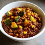Close-up of a white bowl filled with Easy Chili With Corn And Zucchini, showing ground meat, corn kernels, and chunks of green zucchini.