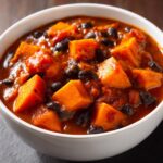 Close-up of a white bowl filled with Easy Sweet Potato And Black Bean Chili, featuring large chunks of orange sweet potato and black beans.