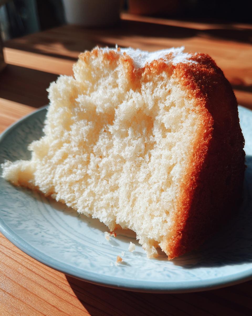 A close-up of a moist, fluffy slice of Vanilla Cake dusted with powdered sugar, sitting on a blue patterned plate.