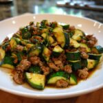 A close-up of a serving of Ground Turkey And Zucchini Skillet with browned meat and bright green zucchini chunks in a savory sauce.