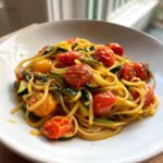 A close-up of Healthy Tomato Zucchini Pasta featuring linguine, blistered cherry tomatoes, and sliced zucchini in a white bowl.