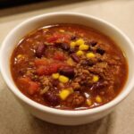 Close-up of a white bowl filled with rich, hearty Taco Soup containing ground meat, kidney beans, corn, and tomatoes.