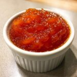 Close-up of thick, vibrant orange-red homemade Sweet And Sour Sauce served in a small white fluted ramekin.
