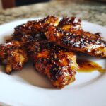 Close-up of sticky, caramelized Honey Garlic Chicken wings sprinkled with sesame seeds on a white plate.