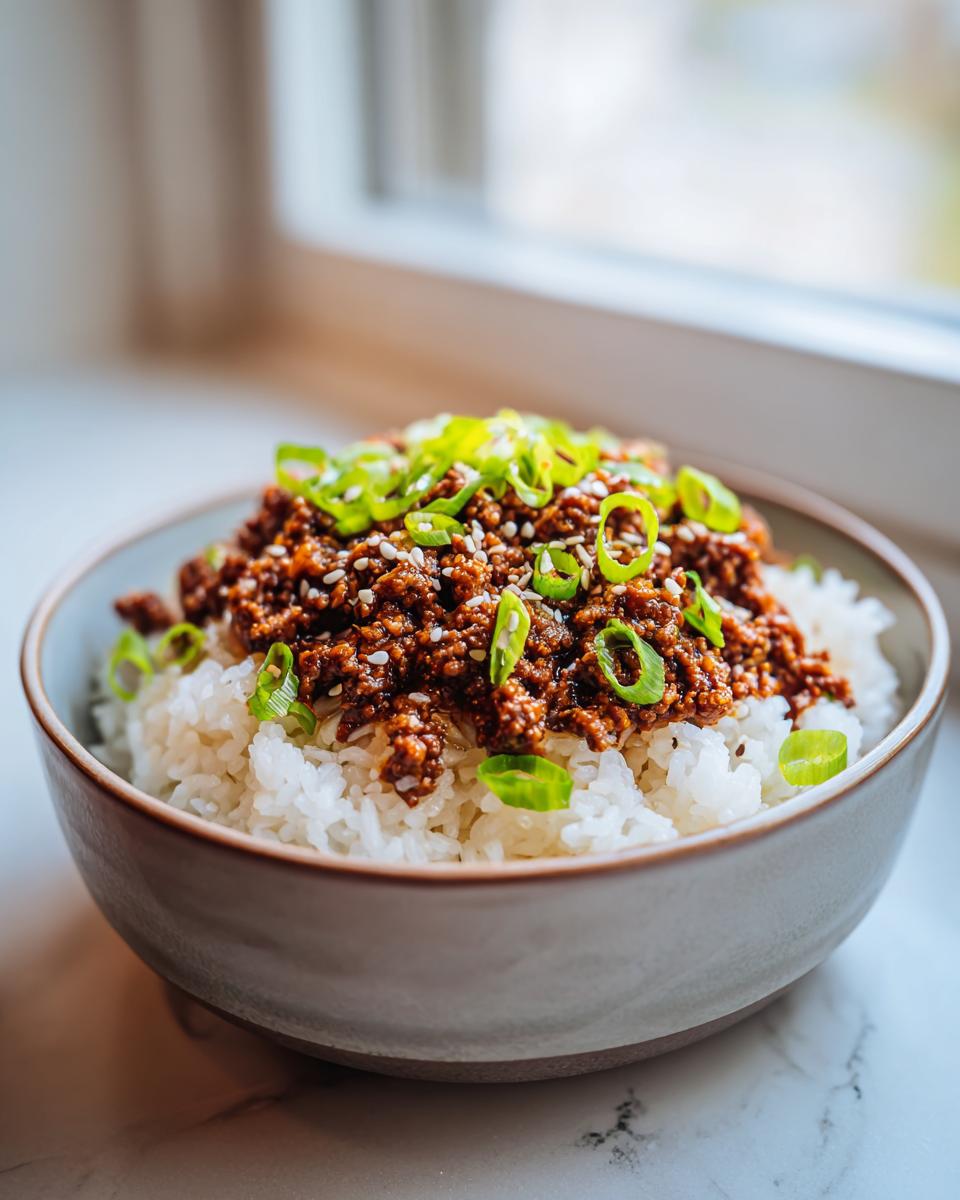 Close-up of a serving of Korean Beef Bowl featuring savory ground beef over white rice, topped with sliced green onions and sesame seeds.