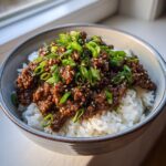 A close-up of a Korean Beef Bowl featuring savory ground beef over white rice, topped generously with sliced green onions and sesame seeds.