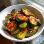Close-up of vibrant Korean Cucumber Salad slices coated in spicy red chili flakes and sauce in a white bowl.