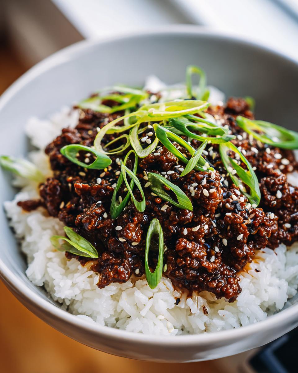 A close-up view of a Korean Ground Beef Bowl featuring savory ground beef served over white rice and topped with sliced green onions and sesame seeds.