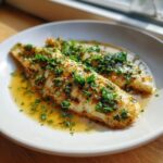Two perfectly cooked Lemon Garlic Butter Tilapia fillets swimming in a rich sauce and topped with fresh chopped parsley.
