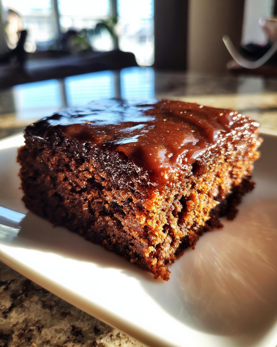 Close-up of a rich, moist slice of Texas Sheet Cake topped with glossy chocolate icing, catching sunlight.