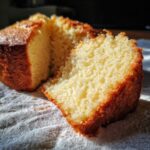 Close-up of a freshly baked Vanilla Cake with a slice pulled away, showing the moist, yellow crumb texture.