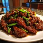 A close-up, appetizing photo of sticky, dark brown Mongolian Beef pieces garnished generously with bright green scallions.