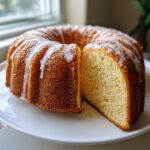 A golden-brown Bundt Cake with white glaze drizzled over the top, featuring one slice cut out to show the moist interior.