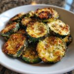 A close-up of crispy, golden Roasted Parmesan Zucchini slices piled high in a white bowl.