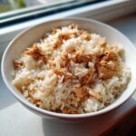 A close-up of fluffy white rice topped with seasoned, shredded chicken in a white bowl.