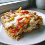 A close-up of a serving of Chicken Fajita Casserole topped with melted cheese and colorful bell peppers.