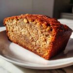 Close-up of a moist slice of Grandma Banana Nut Bread with visible nuts on a white plate.