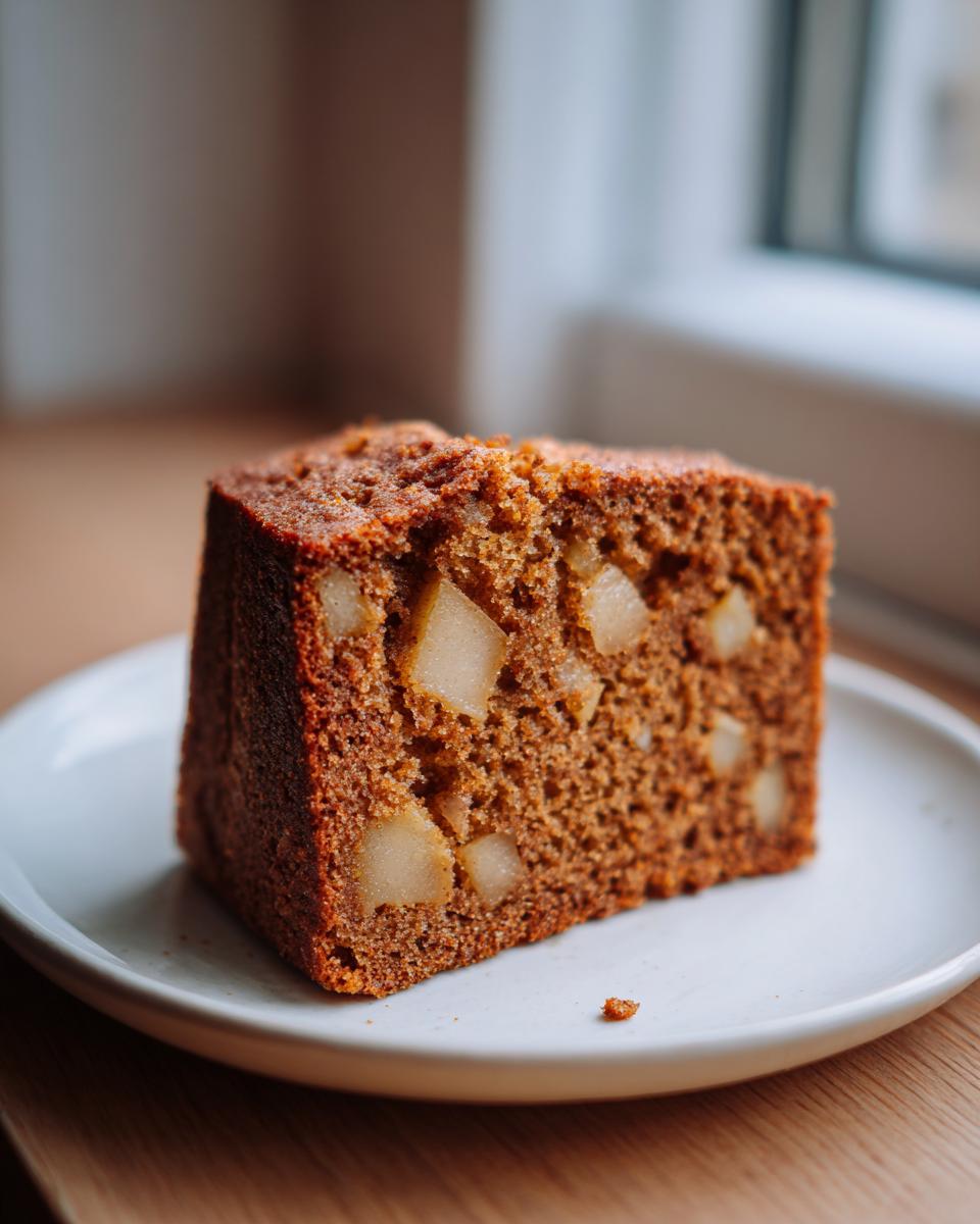 Close-up of a moist slice of Spiced Pear Cake showing chunks of baked pear throughout the dark brown crumb.