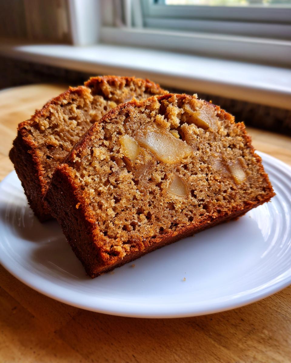 Two thick slices of moist Spiced Pear Cake showing chunks of pear baked into the rich brown crumb, served on a white plate.