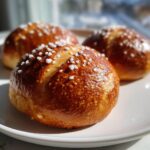 Three freshly baked Soft Pretzel Buns with a deep brown, glossy crust and coarse salt topping.