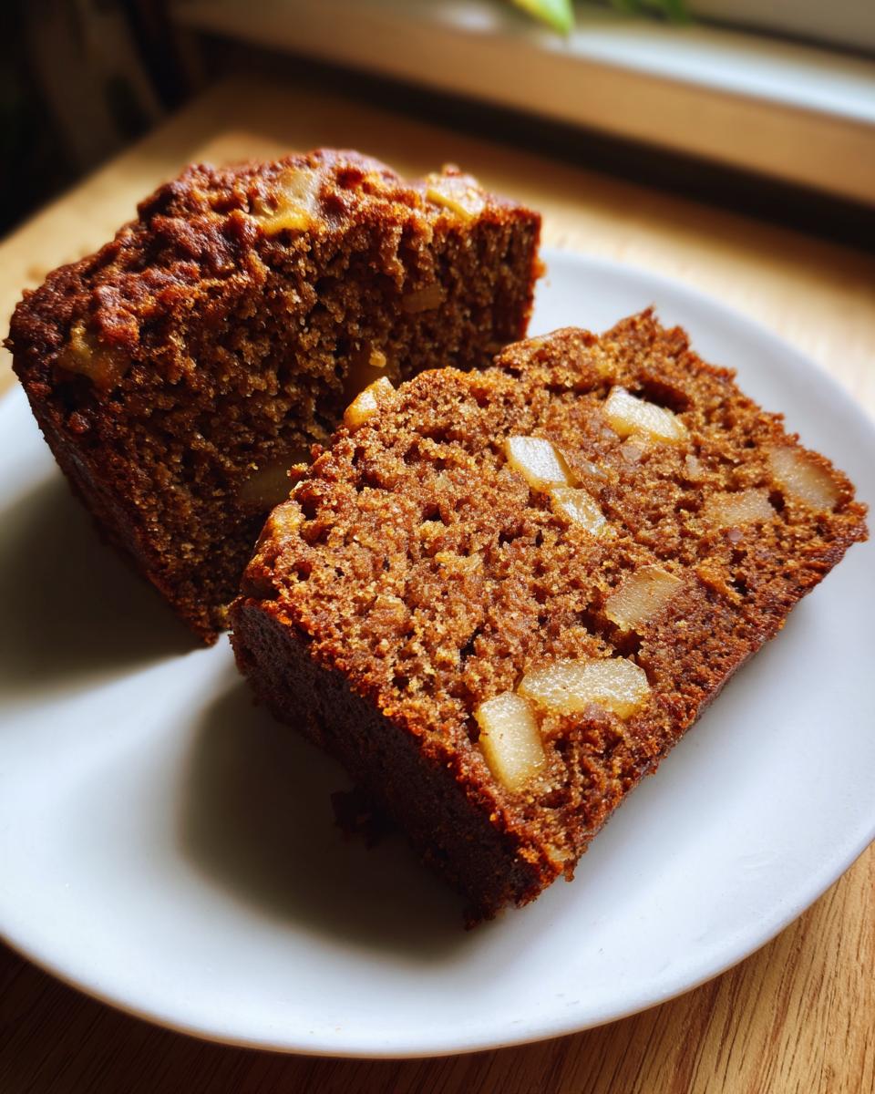 Two slices of dark, moist Spiced Pear Cake showing visible chunks of pear baked inside, served on a white plate.
