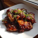 Close-up of sticky, glazed Teriyaki Chicken pieces garnished with sesame seeds and sliced green onions.