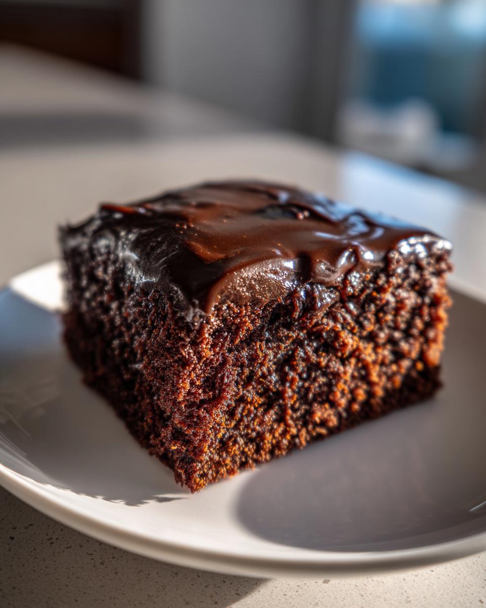 A close-up, richly textured slice of Texas Sheet Cake topped with glossy, melted chocolate frosting.