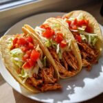 Three crispy shell Chicken Tacos filled with shredded seasoned chicken, lettuce, and diced tomatoes.