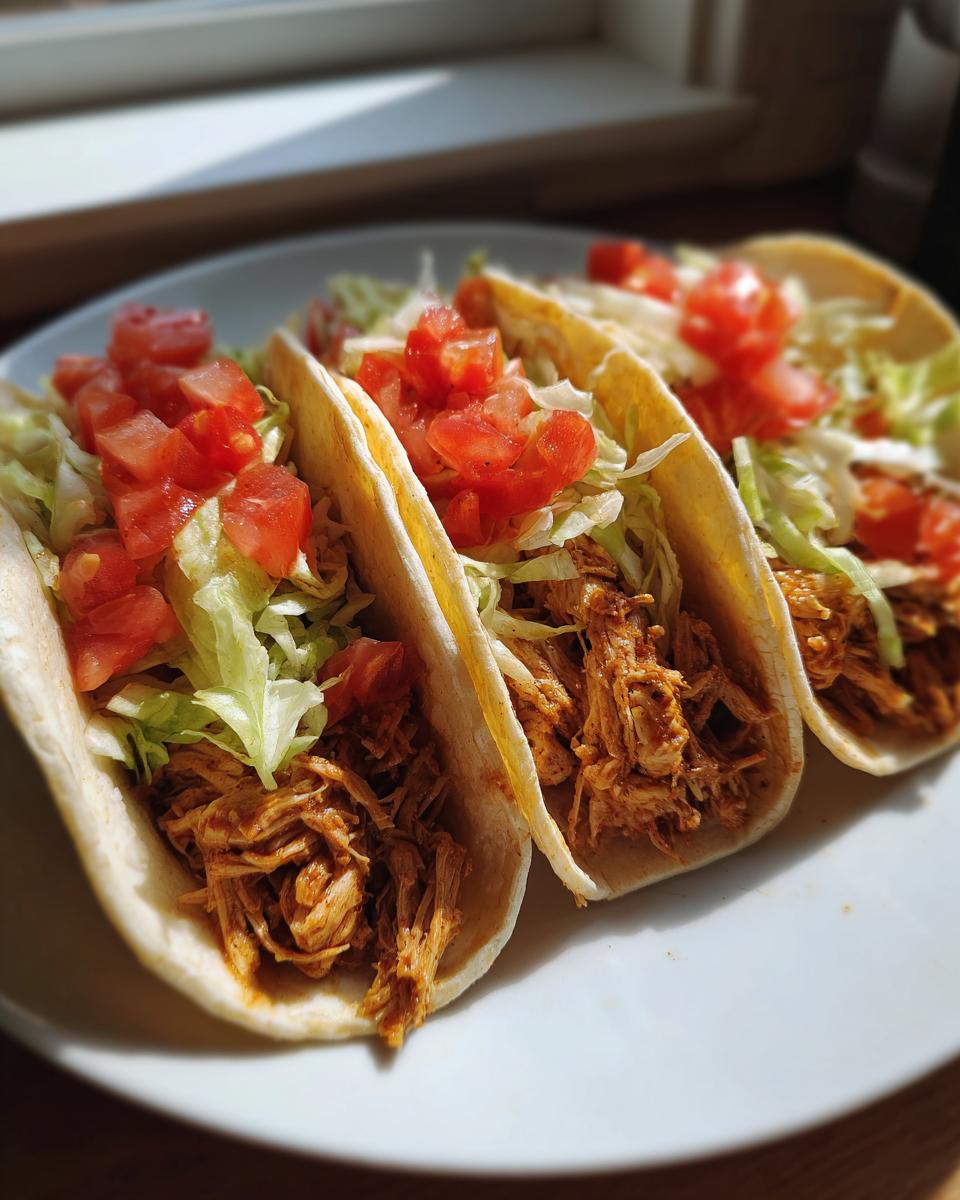 Three soft shell Chicken Tacos filled with shredded seasoned chicken, lettuce, and diced tomatoes.