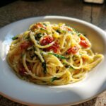A close-up of a white bowl filled with Tomato Zucchini Pasta, topped with grated cheese.