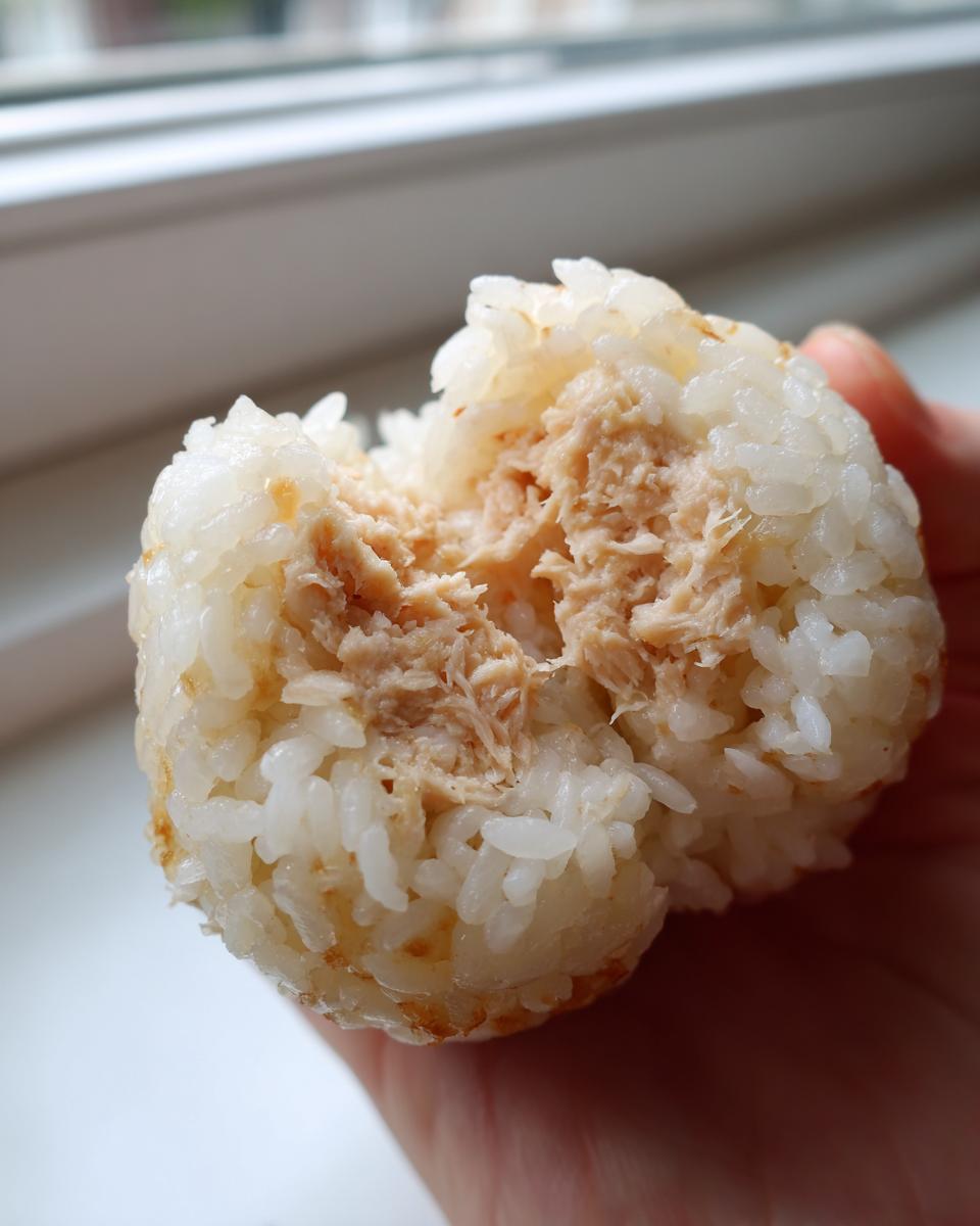 A close-up view of a Tuna Mayo Rice Balls being held, showing the fluffy white rice exterior and the savory tuna filling inside.
