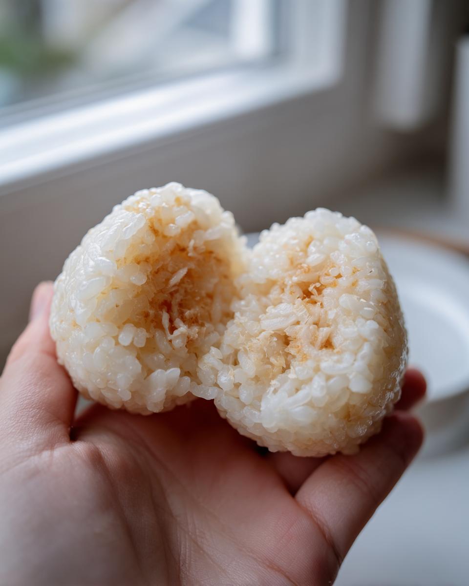 A hand holding a Tuna Mayo Rice Balls cut in half, showing the creamy tuna filling inside the sticky rice.