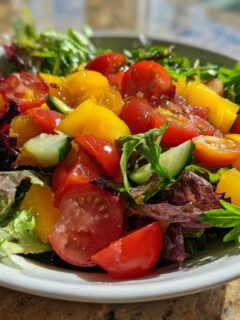 Close-up of a vibrant summer salad featuring mixed greens, red and yellow cherry tomatoes, and cucumber slices.