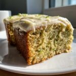 Close-up of a moist slice of Zucchini Cake With Cream Cheese frosting, showing green flecks of zucchini.