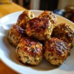 A close-up of several perfectly browned Air Fryer Turkey Meatballs seasoned with herbs, served on a white plate.