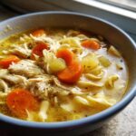 Close-up of a bowl of amazing 15-min chicken soup with shredded chicken, carrots, and egg noodles in broth.