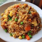 Close-up of a generous serving of savory Chicken Fried Rice featuring rice, scrambled egg, peas, carrots, and browned chicken pieces.