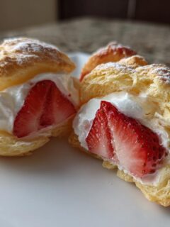 Close-up of two halves of Strawberry Cream Puffs filled with whipped cream and fresh strawberry slices, dusted with powdered sugar.