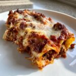 Close-up of a serving of baked meat Cannelloni Recipes covered in rich tomato sauce and melted, browned cheese.